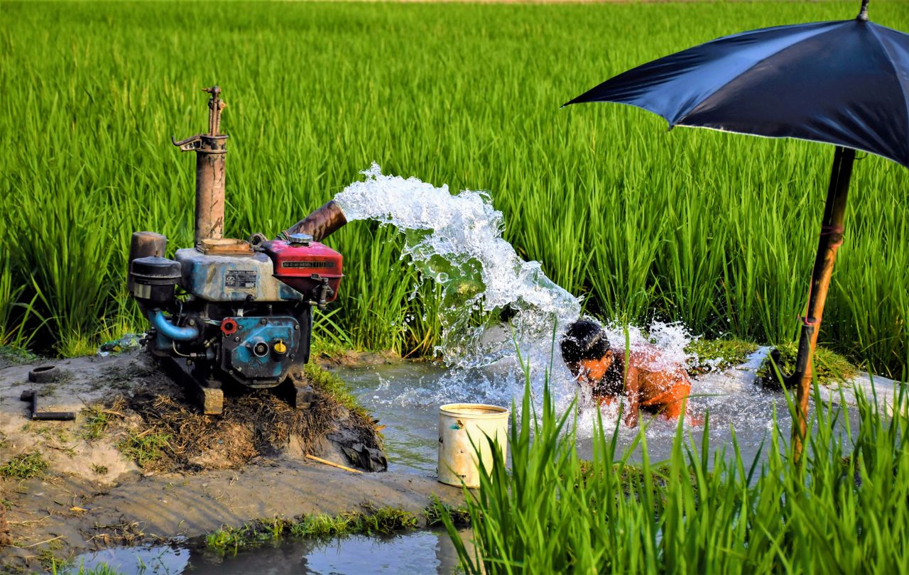 Rural irrigation scene with a child enjoying water from a pump in Bangladesh.